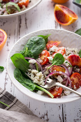 Healthy spring salad with quinoa, fresh spinach and blood oranges on white rustic background