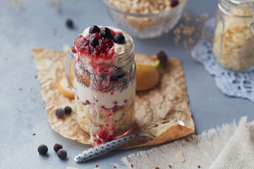 Layered dessert with muesli, yogurt, banana, linen seeds, slised almonds and berries in glass mason jar on blue rustic background.