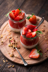 Delicious homemade granola, yogurt and strawberry parfait in glass jars on rustic wooden background