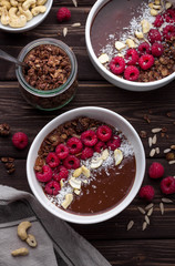 Obraz na płótnie Canvas Chocolate breakfast bowls with frozen banana, cocoa, granola, raspberries, cashew nuts and coconut. Overhead shot