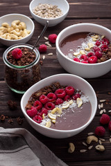 Breakfast bowls with frozen banana, cocoa, raspberries, coconut and nuts on rustic wooden background