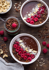Chocolate breakfast bowls with frozen banana, cocoa, granola, raspberries, cashew nuts and coconut. Overhead shot