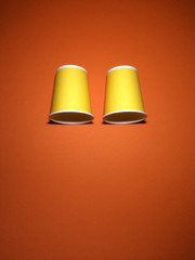 Two yellow disposable cups on orange textured paper background with copy space.