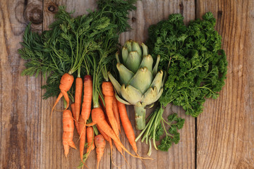 Small carrots, artichoke and bouquet of parsley on an old wooden table