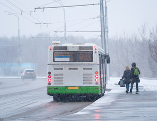 Modern city bus on bus stop with passengers enter inside in snow winter day