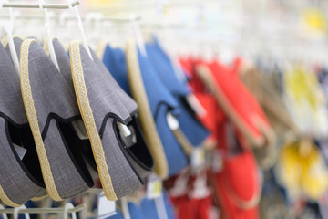 Rows of hangers with modern casual shoes of different colours in shoes store on blurry background
