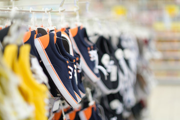 Rows of hangers with sneakers of different colours in shoes store on blurry background