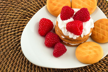 Fresh Red Raspberries on a white artistic plate / Red Fresh Raspberries on a white artistic plate with cookies, rosemary, chocolate and cream in the background.