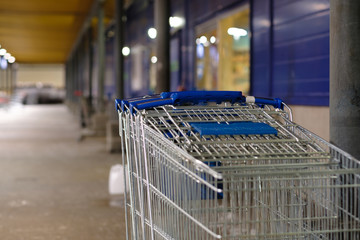 Row of stacked shopping carts with blue handles near exit of supermarket in night