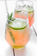 glass of fresh juice with lime and rosemary on wooden table background