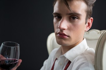 Androgynous man holding wine glass against black background