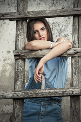 Portrait of beautiful young woman standing in front of rustic wall and leaning on a ladder