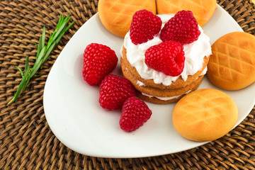 Fresh Red Raspberries on a white artistic plate / Red Fresh Raspberries on a white artistic plate with cookies, rosemary, chocolate and cream in the background.