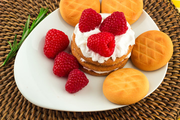 Fresh Red Raspberries on a white artistic plate / Red Fresh Raspberries on a white artistic plate with cookies, rosemary, chocolate and cream in the background.
