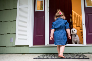 Rear view of young girl walking towards open door with dog waiting