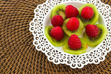 Fresh Red Raspberries on a white artistic plate / Red Fresh Raspberries on a white artistic plate with cookies, rosemary, chocolate and cream in the background.