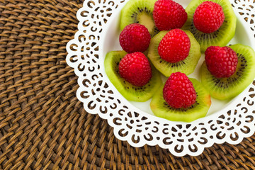 Fresh Red Raspberries on a white artistic plate / Red Fresh Raspberries on a white artistic plate with cookies, rosemary, chocolate and cream in the background.