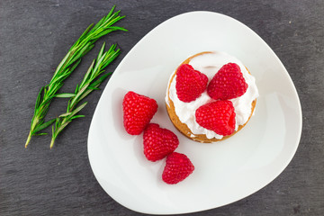 Fresh Red Raspberries on a white artistic plate / Red Fresh Raspberries on a white artistic plate with cookies, rosemary, chocolate and cream in the background.