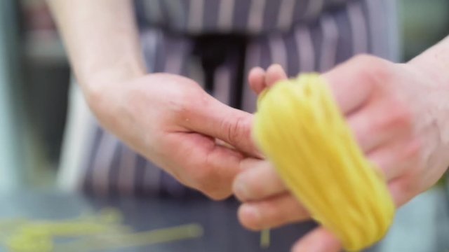 Coiling pasta into the nest. Chef to wind up a paste on his hand, it turns a nest. Slow mo. Close up