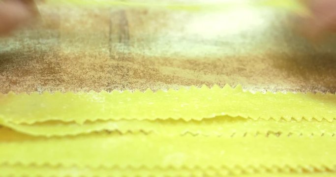Mens hands lay out in a row thinly sliced pasta macaroni with a wavy edge on the table, timelapse, close up