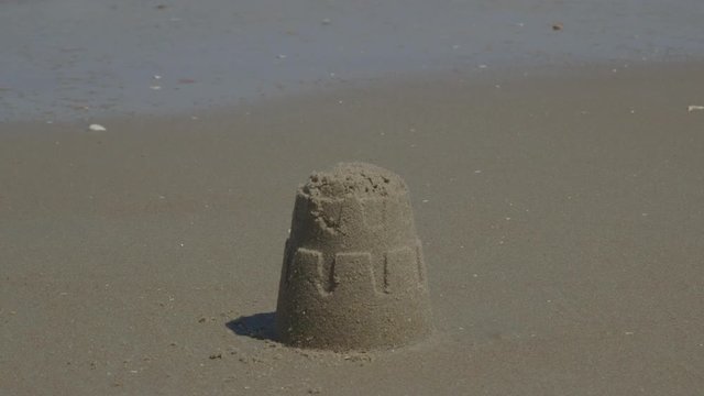 Ocean Waves Destroying Small Sandcastle on the Beach