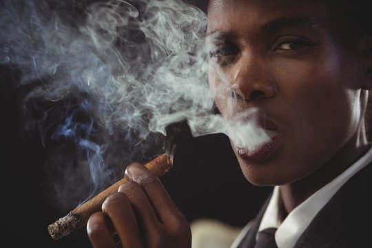 Androgynous man smoking cigar while sitting on a chair