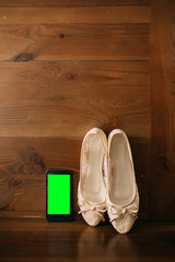 Fototapeta na wymiar Cream bride shoes on a wooden background and phone with a green screen. Wedding in Montenegro.