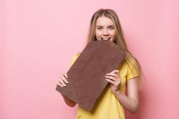 Woman with chocolate smiling. Cute girl holding and eating giant cocoa chocolate bar near pink wall. - 145184565
