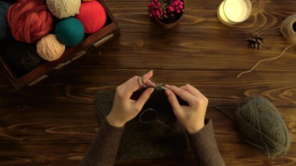 Woman knitting with crochet hook on wooden desk background. Green thread. Top view