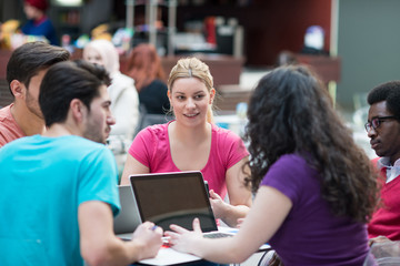 A group of teenagers sitting at the table in cafe, using laptop and drinking orange juice.