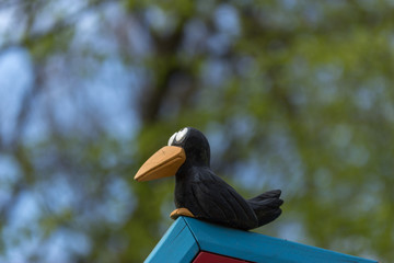Wood carved crow sit on a roof with a forest as background