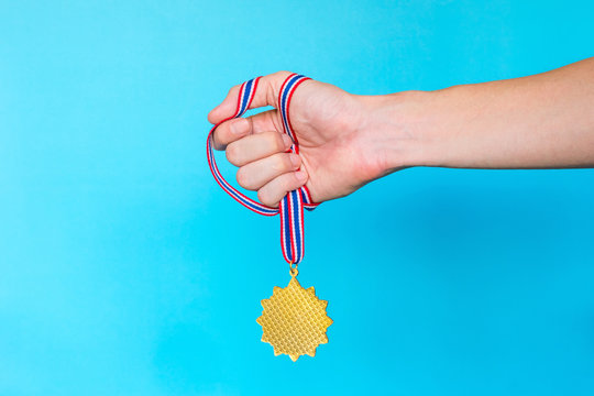 Hand holding Gold medal with ribbon on blue background. - Powered by Adobe