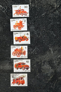 Set of lying in a row postage stamps printed in Cuba shows fire engines, series, circa 1977. Copy space for your text on a dark black cement background.