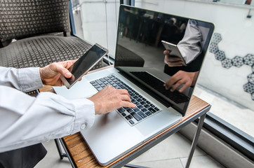 Portrait of young man with mobile phone working on laptop at indoor coffee shop