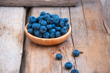 Heap of fresh ripe raw bluberries in a small wooden plate on a wooden background. Rustic style and copy space.