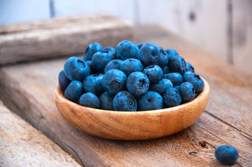 Heap of fresh ripe raw bluberries in a small wooden plate on a wooden background. Rustic style and copy space.