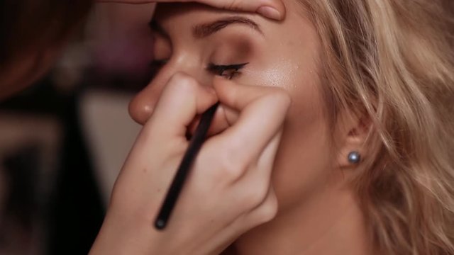 The girl make-up artist traces the line of the eyelashes on the eye of the model.
