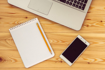 Smartphone, laptop computer and blank paper on wooden background