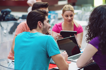 A group of teenagers sitting at the table in cafe, using laptop and drinking orange juice.