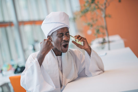 Sudanese Business Man In Traditional Outfit Using Mobile Phone In Office