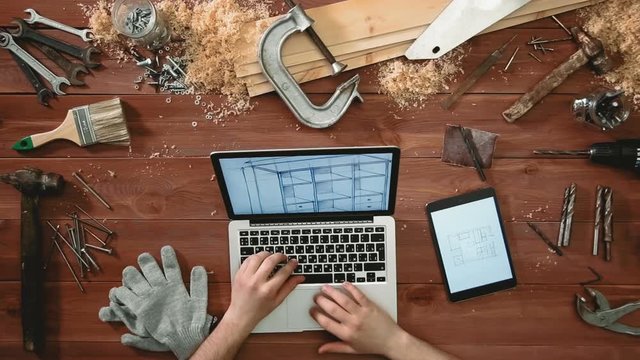 Top view craftsman hands using laptop computer and digital tablet looking at sketches with floor plan