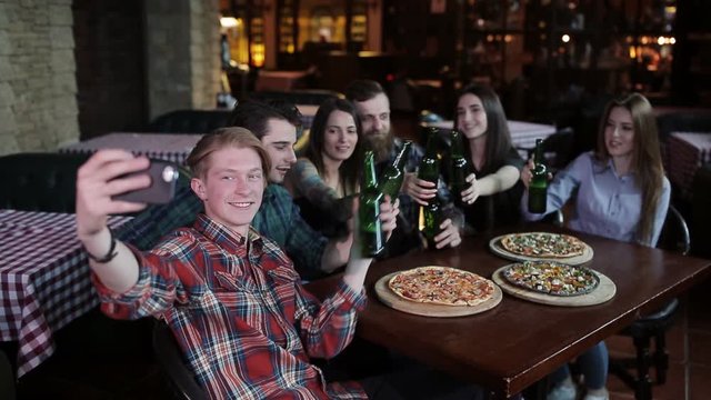 The guy makes a friend company in pizzeria. A company of friends resting in a pizzeria and making selfie on the background of pizza and beer