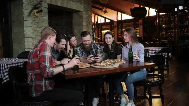 The guy makes a friend company in pizzeria. A company of friends resting in a pizzeria and making selfie on the background of pizza and beer
