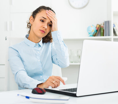 Exhausted young woman working at laptop