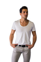 Fototapeta premium Brown eyed, black haired latin man standing in studio, looking to a side, hands in pockets, isolated on white background