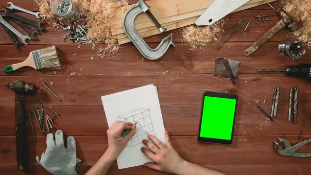 Top view craftsman hands drawing a sketch of cabinet, digital tablet green screen lying on desk