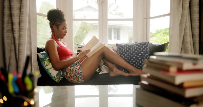 Happy female student reading book and sitting on sofa. Young african american woman relaxing, black girl lying on couch. Hispanic people and lifestyle, leisure and relaxation at home

