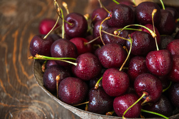Sweet fresh ripe burgundy cherries with water drops in a bowl on a wooden background. Close up and copy space.