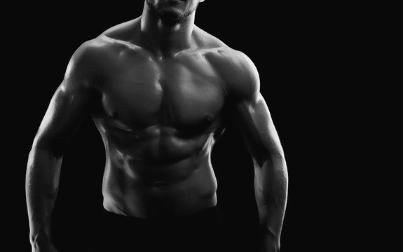 Horizontal cropped black and white studio shot of a muscular sexy torso of an athletic man posing shirtless on black background copyspace fitness strength athletics power sports bodybuilding concept.