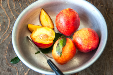 Close up of whole and slices of fresh ripe honeyed nectarines (peaches) with leaves and water drops in a vintage bowl on a wooden board. Summer fruits concept. Rustic style.